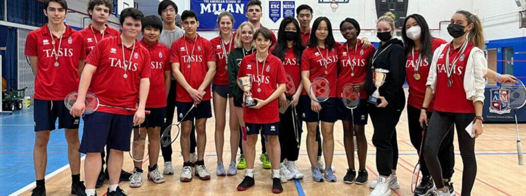 Young students from World Schools celebrating a badminton victory in a gymnasium, showcasing sports excellence and diverse student achievements.