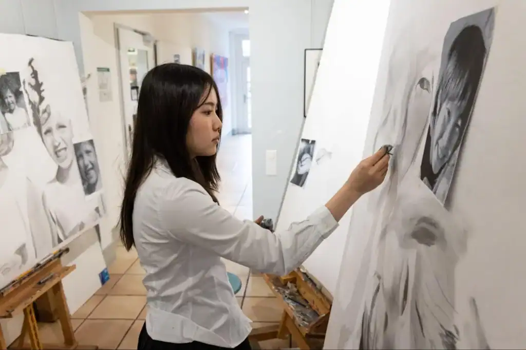 Young female student drawing realistic portrait art in classroom at an international school.