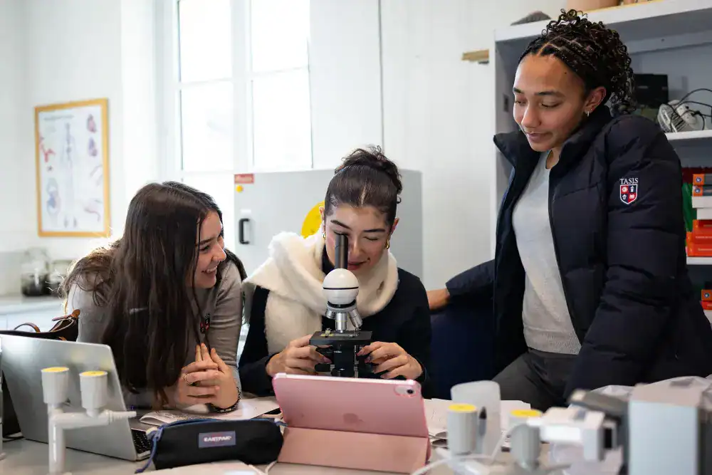 This Month at TASIS: January 2025 9 Diverse students conducting scientific research with microscope at school lab.