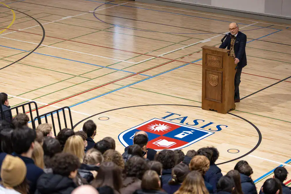 This Month at TASIS: March 2025 10 Modern indoor school gymnasium with a speaker at podium and attentive audience, representing World Schools education event.