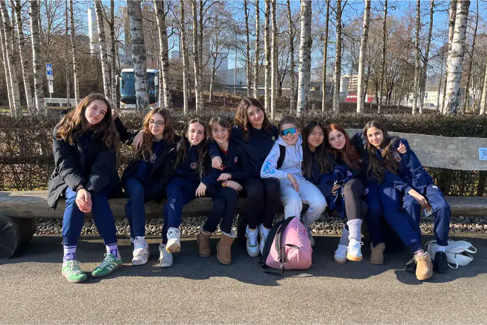 This Month at TASIS: March 2025 7 Girls school trip outdoors, students sitting on a bench in winter, exploring education at World Schools.