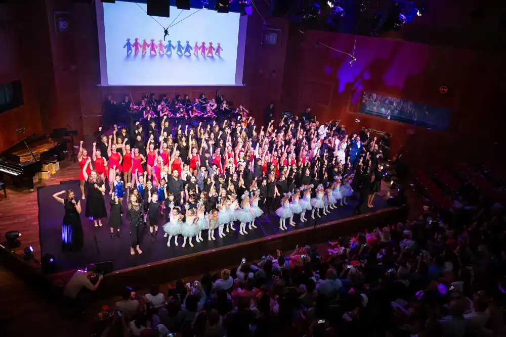 This Year at TASIS: 2024 17 Diverse students performing on stage with orchestra at world schools event.