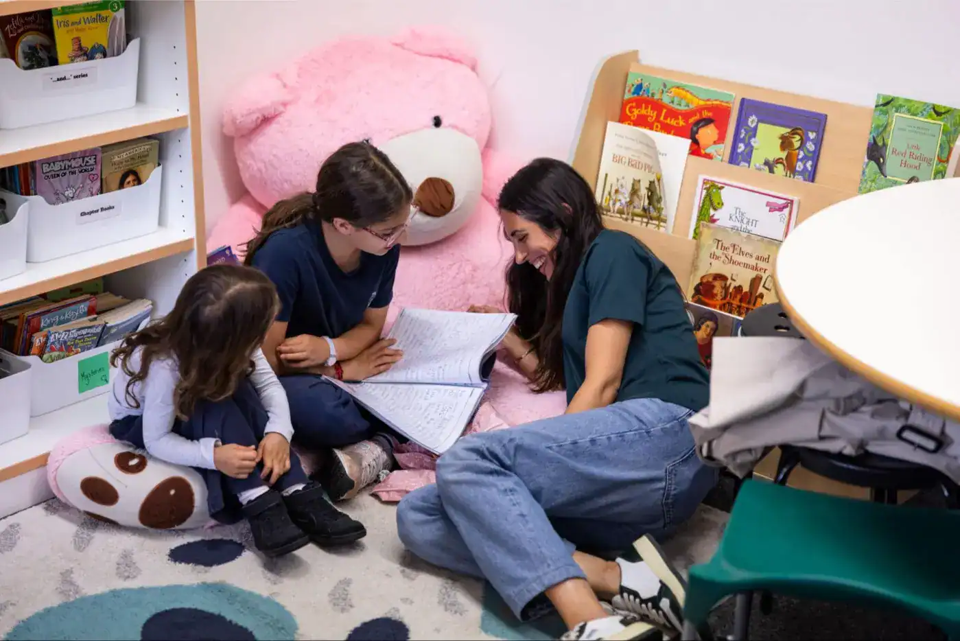 This Month at TASIS: June 2025 2 Cute children and teacher reading book in cozy library reading nook with plush pink bear.