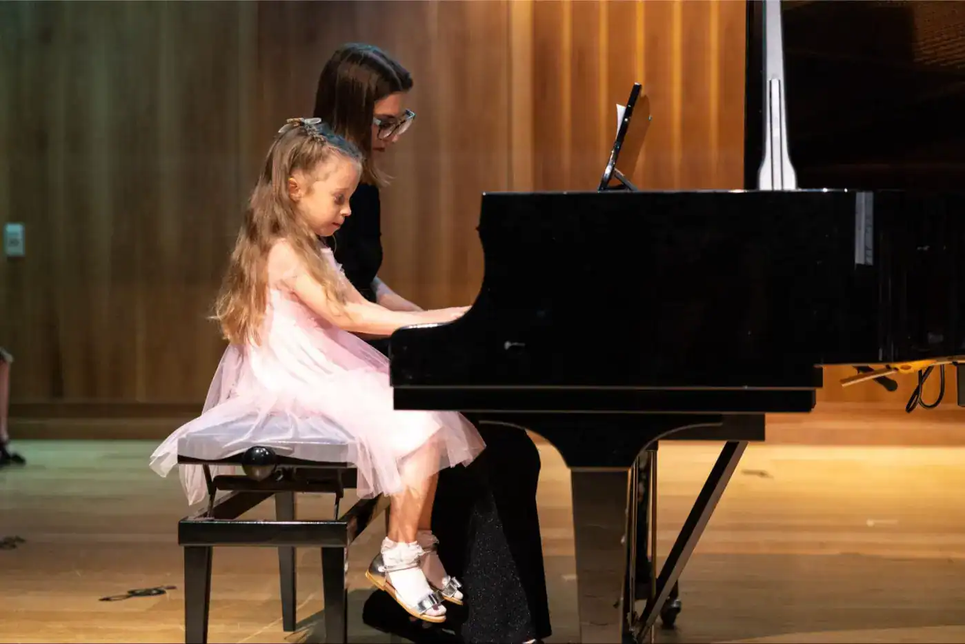 This Month at TASIS: June 2025 3 Young girl and teacher learning piano in school recital.