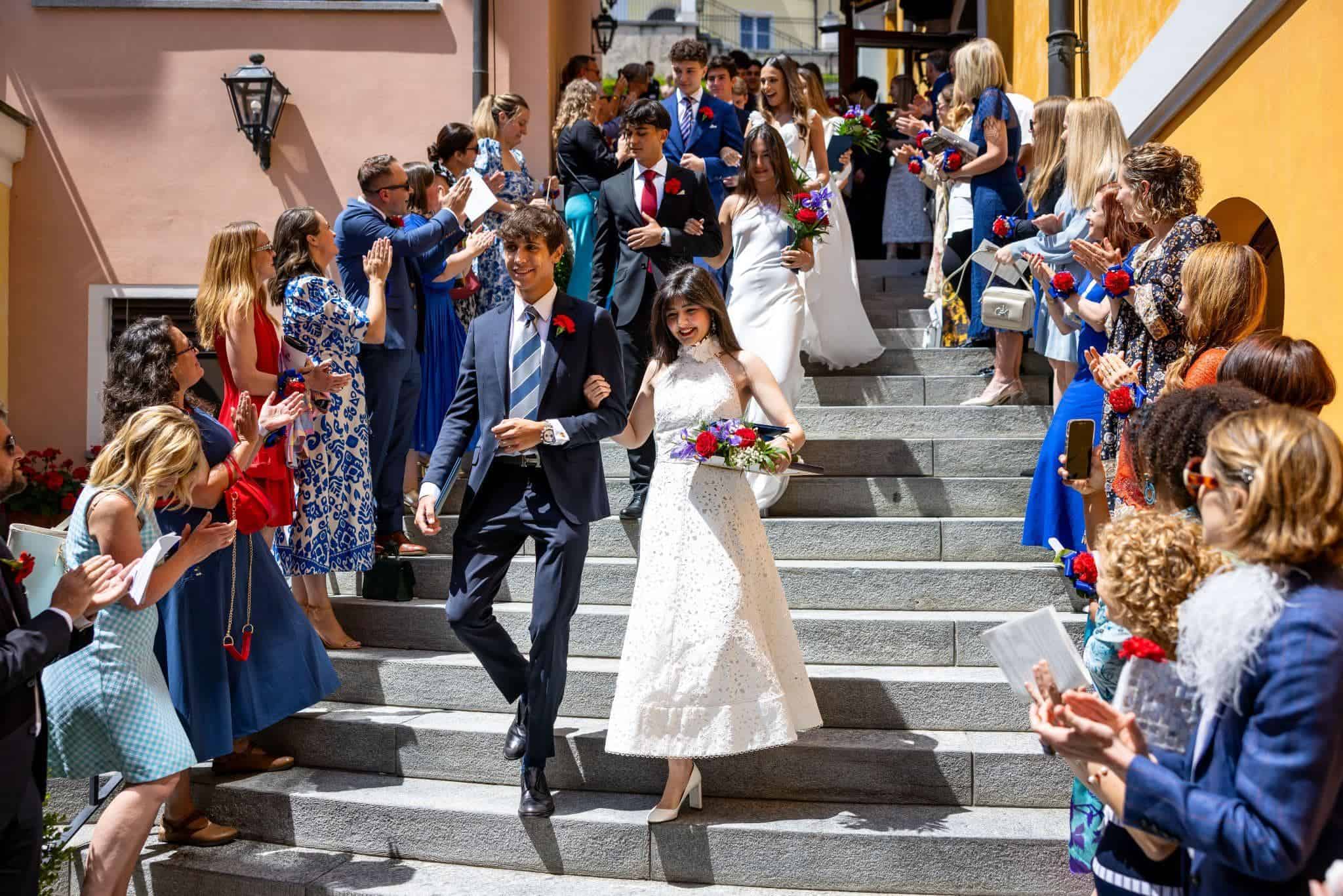 This Month at TASIS: May 2025 24 Graduates exiting the school building during graduation ceremony with family and friends.