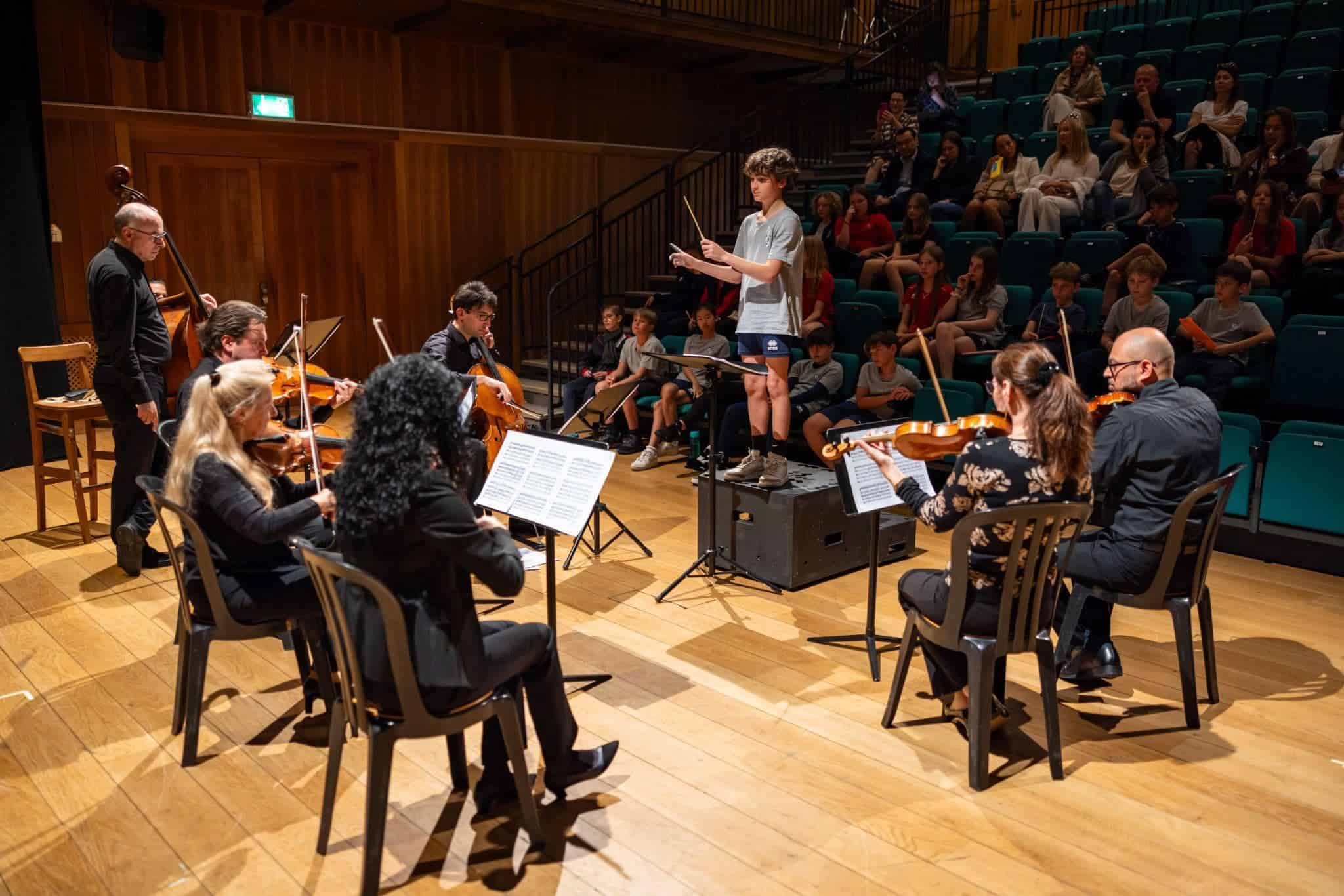 This Month at TASIS: May 2025 11 Young student conducting an orchestra during a school music performance at a world schools event.