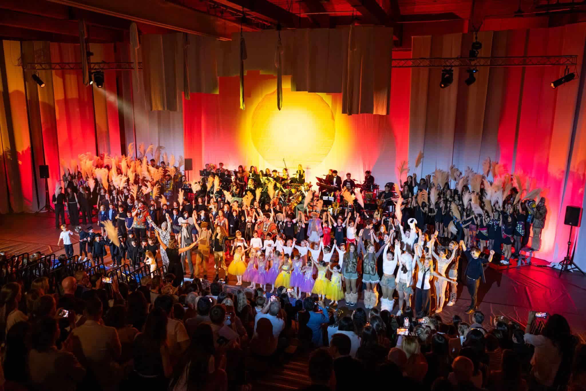 This Month at TASIS: May 2025 15 Vibrant school performance featuring students and orchestra on stage with audience viewing, showcasing excellence in world schools.