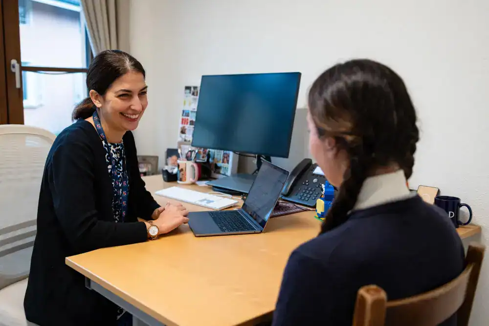 This Month at TASIS: November 2024 11 Motivated teacher and student discussing academic success at a school office.