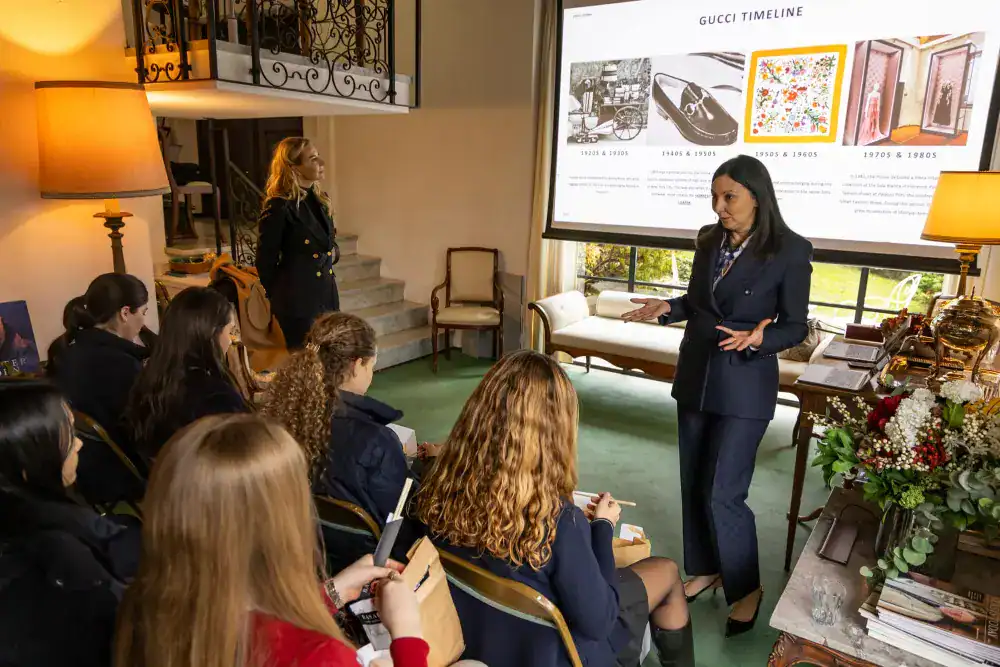 This Month at TASIS: November 2024 17 A woman presents to students in a classroom with a large presentation screen about Gucci's timeline.