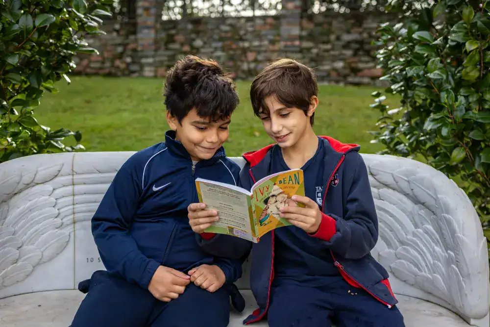 This Month at TASIS: November 2024 5 Bright young boys reading a children's book outdoors, emphasizing education and literacy for world schools.