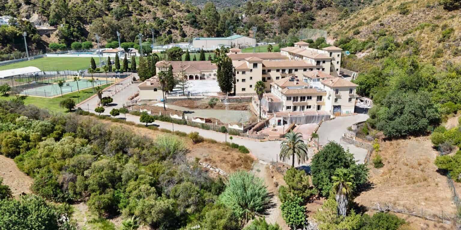 Aerial view of a large modern school campus surrounded by lush greenery and sports facilities.