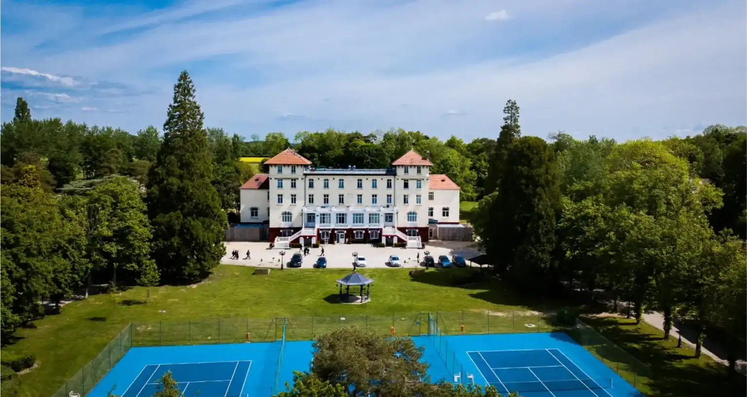 Gorgeous school building surrounded by green trees and tennis courts on a sunny day.