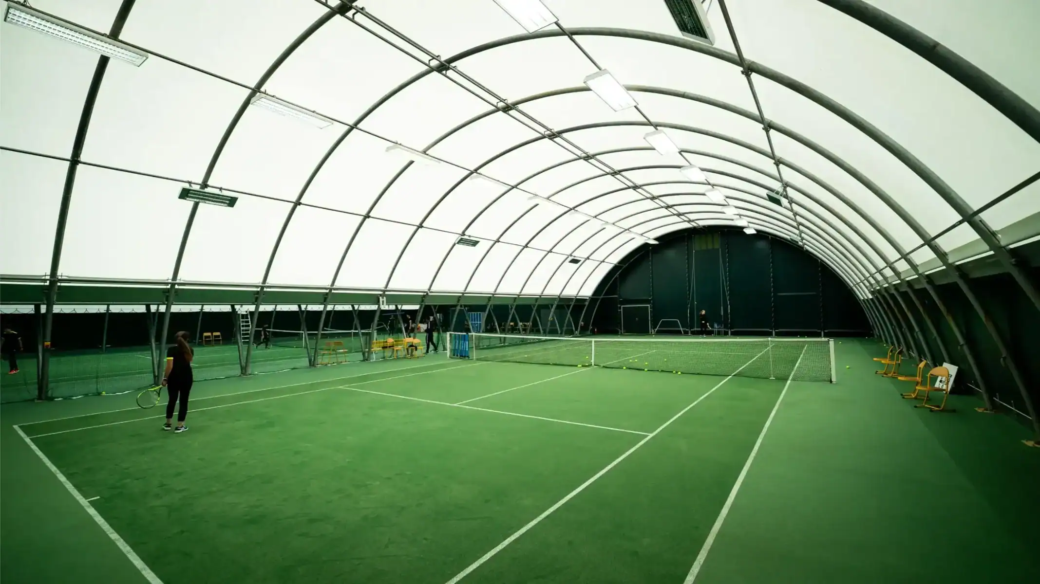 Indoor tennis court with artificial grass surface and high-tech canopy, ideal for school sports facilities.