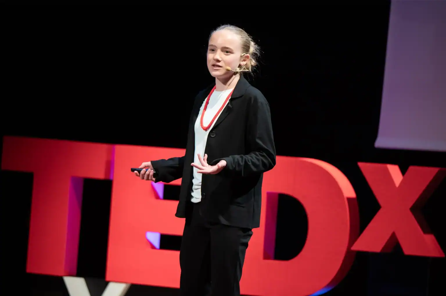 Young girl giving a TEDx talk on stage, promoting innovative education and global school networks.