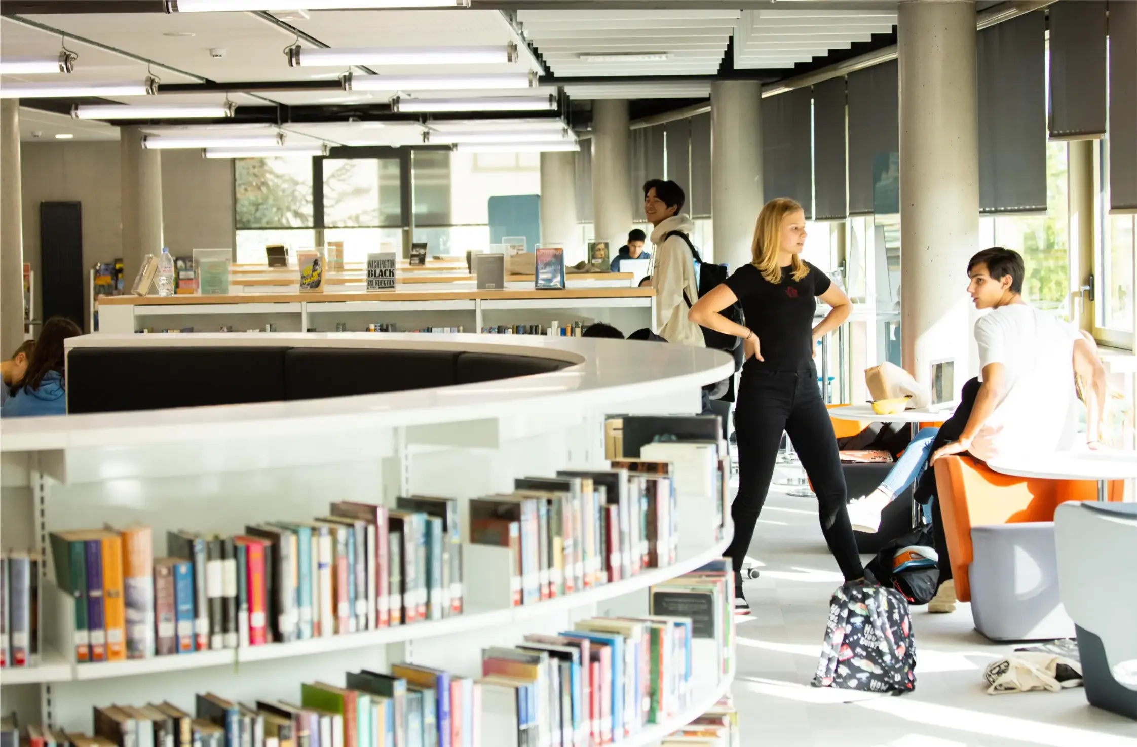 Bright modern school library with students studying, reading, and collaborating.