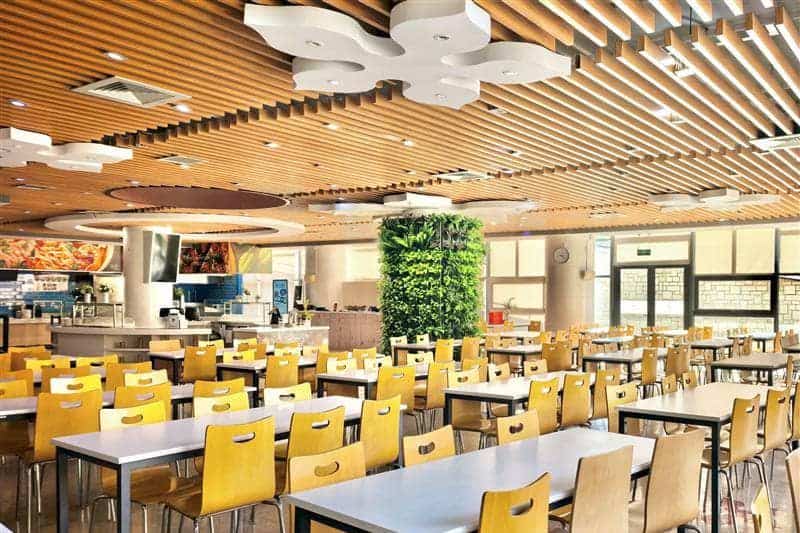 Bright and spacious school cafeteria with yellow chairs and wooden ceiling at Dulwich College Suzhou.