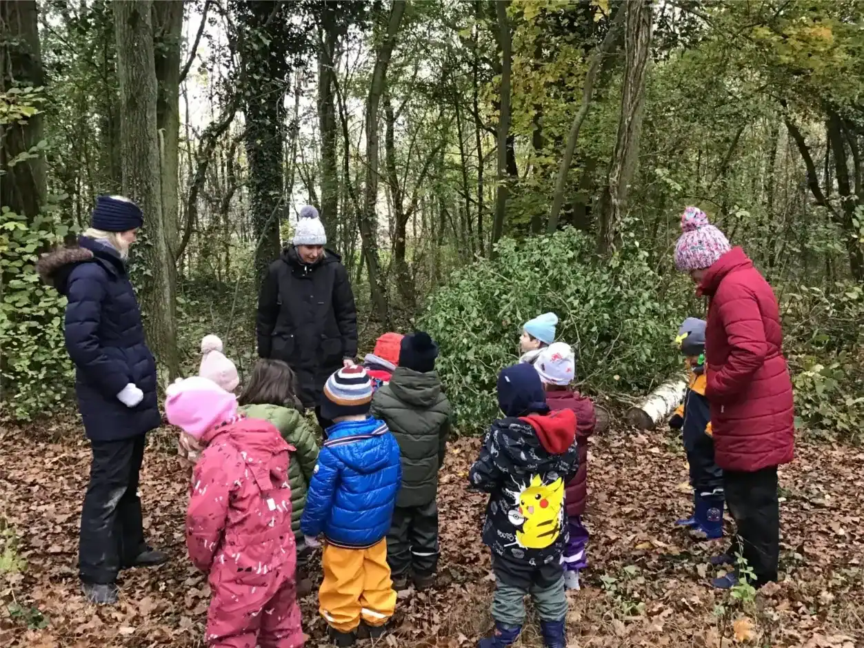 Children engaged in nature exploration with teachers in a wooded area.
