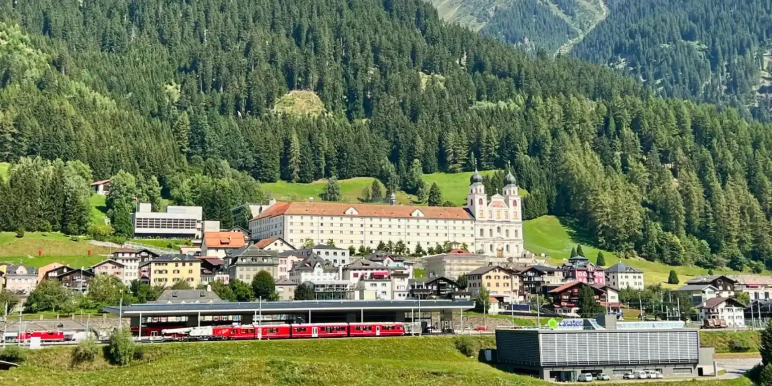 View of Kloster Disentis with school buildings and train in foreground.