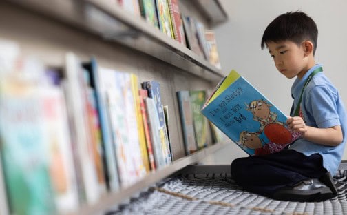 Young student reading a book in the school library at Dulwich College Seoul.