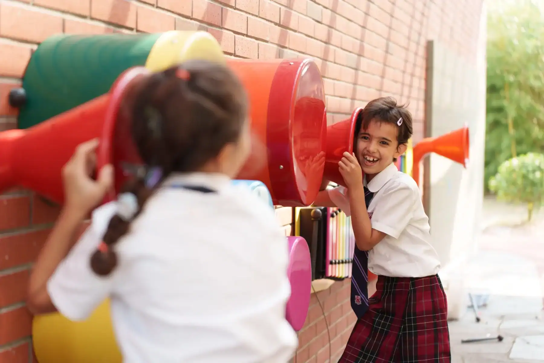 Children playing with colorful musical instruments outside school.