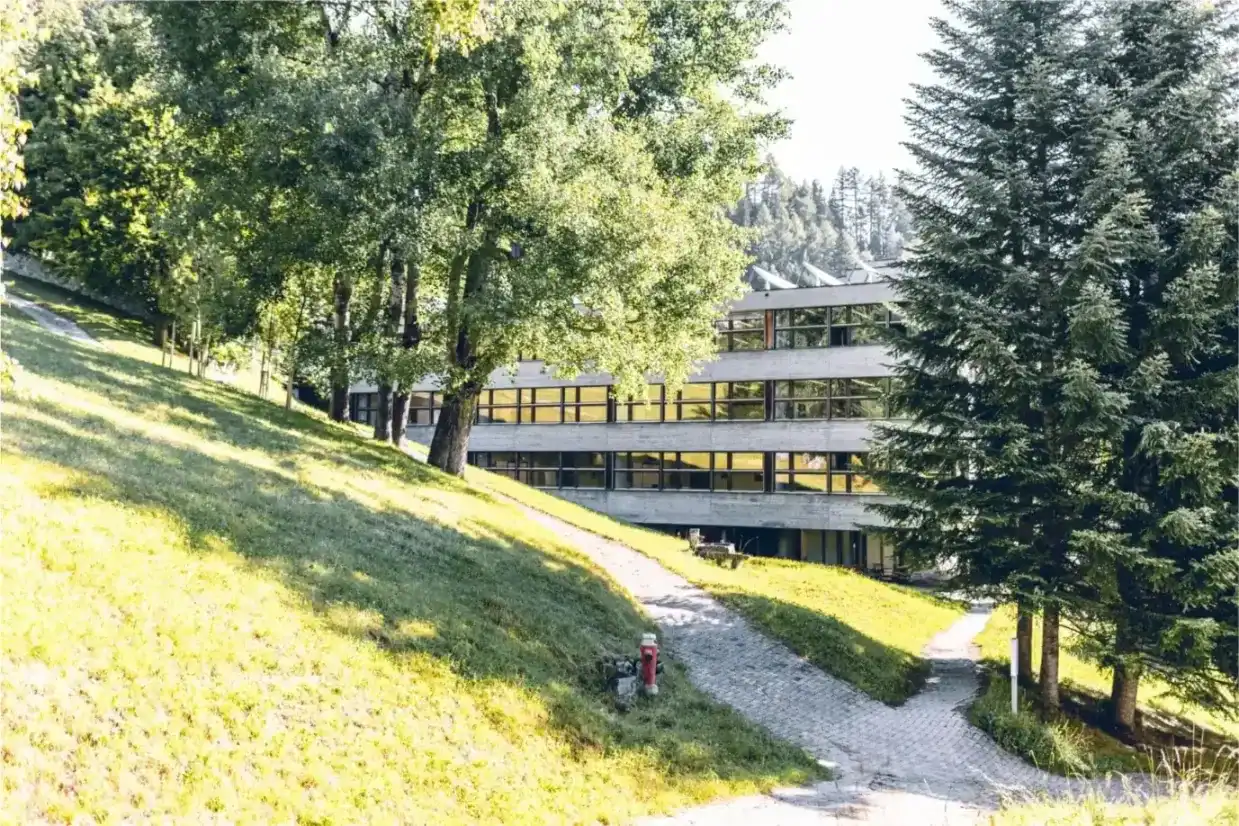 Modern school building at Kloster Disentis surrounded by lush greenery and tall trees.