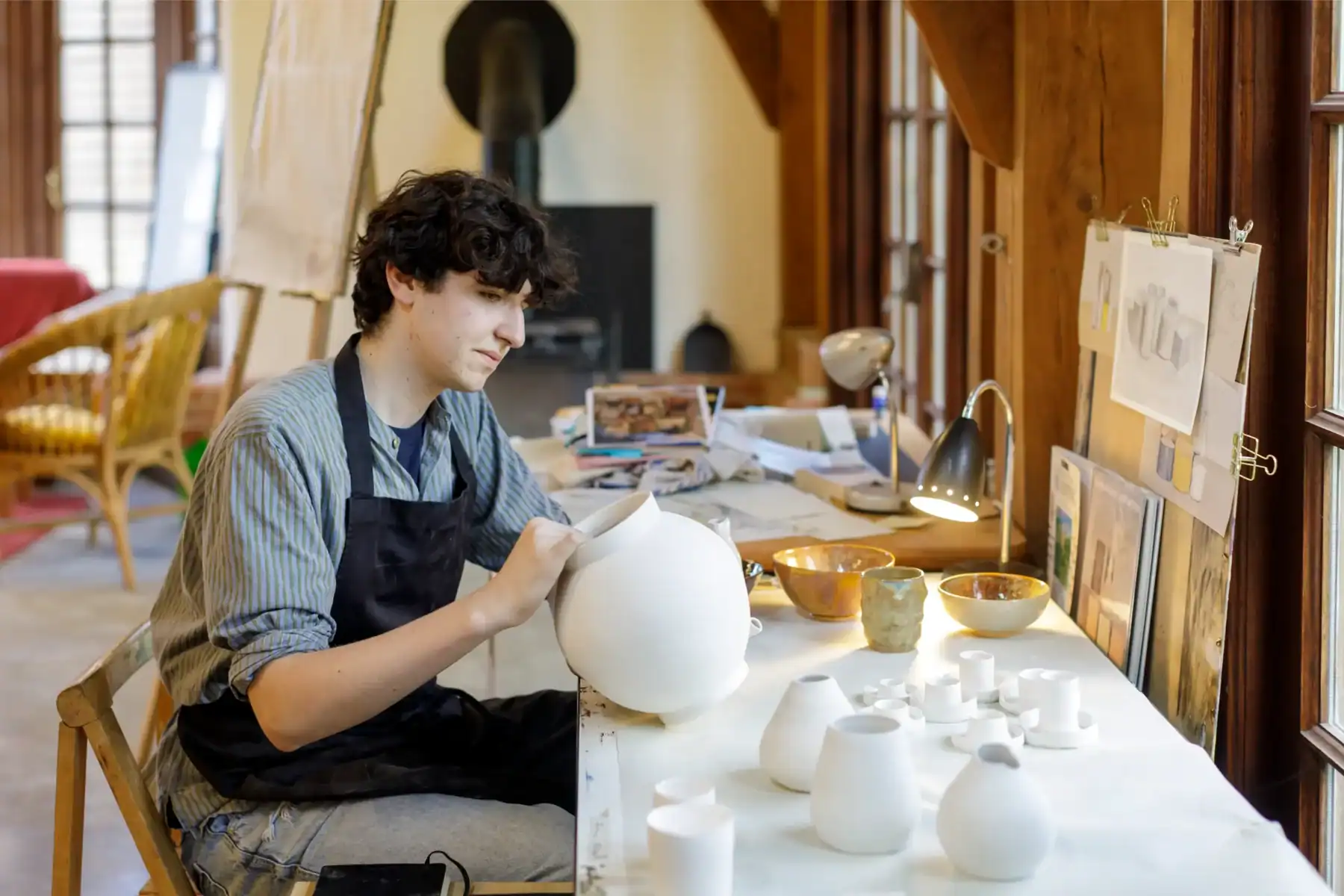 Pottery student shaping clay in a bright, cozy studio with natural light.