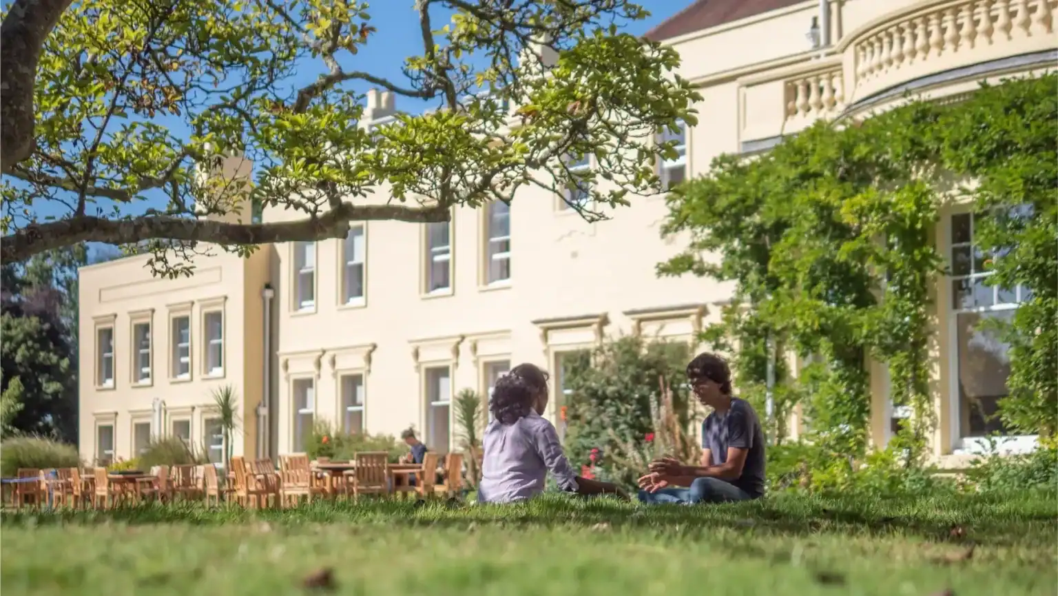 Students sitting on grass in front of Brockwood Park School building.