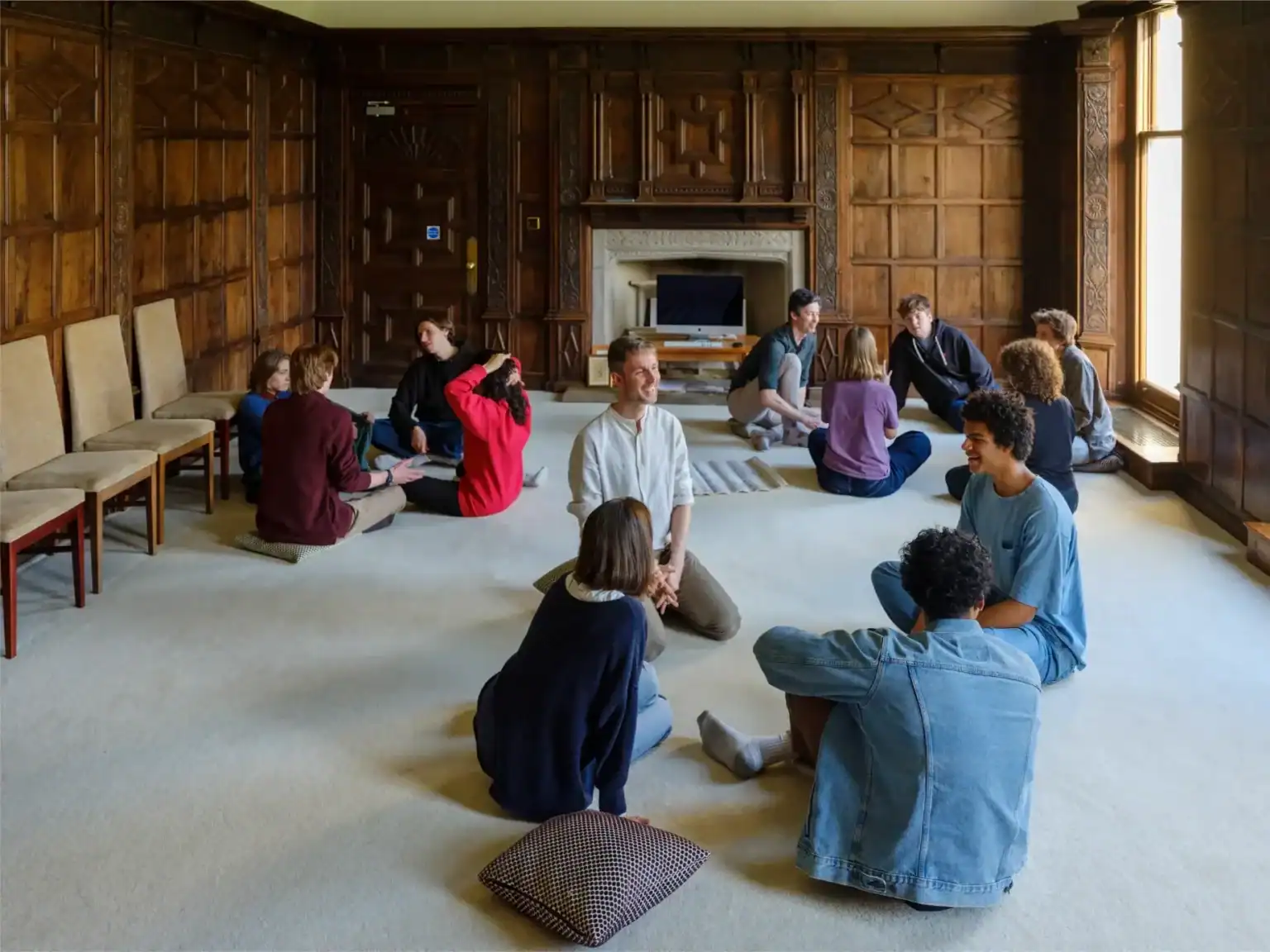 Students practicing mindfulness meditation in a spacious, wood-paneled room at Brockwood Park School.