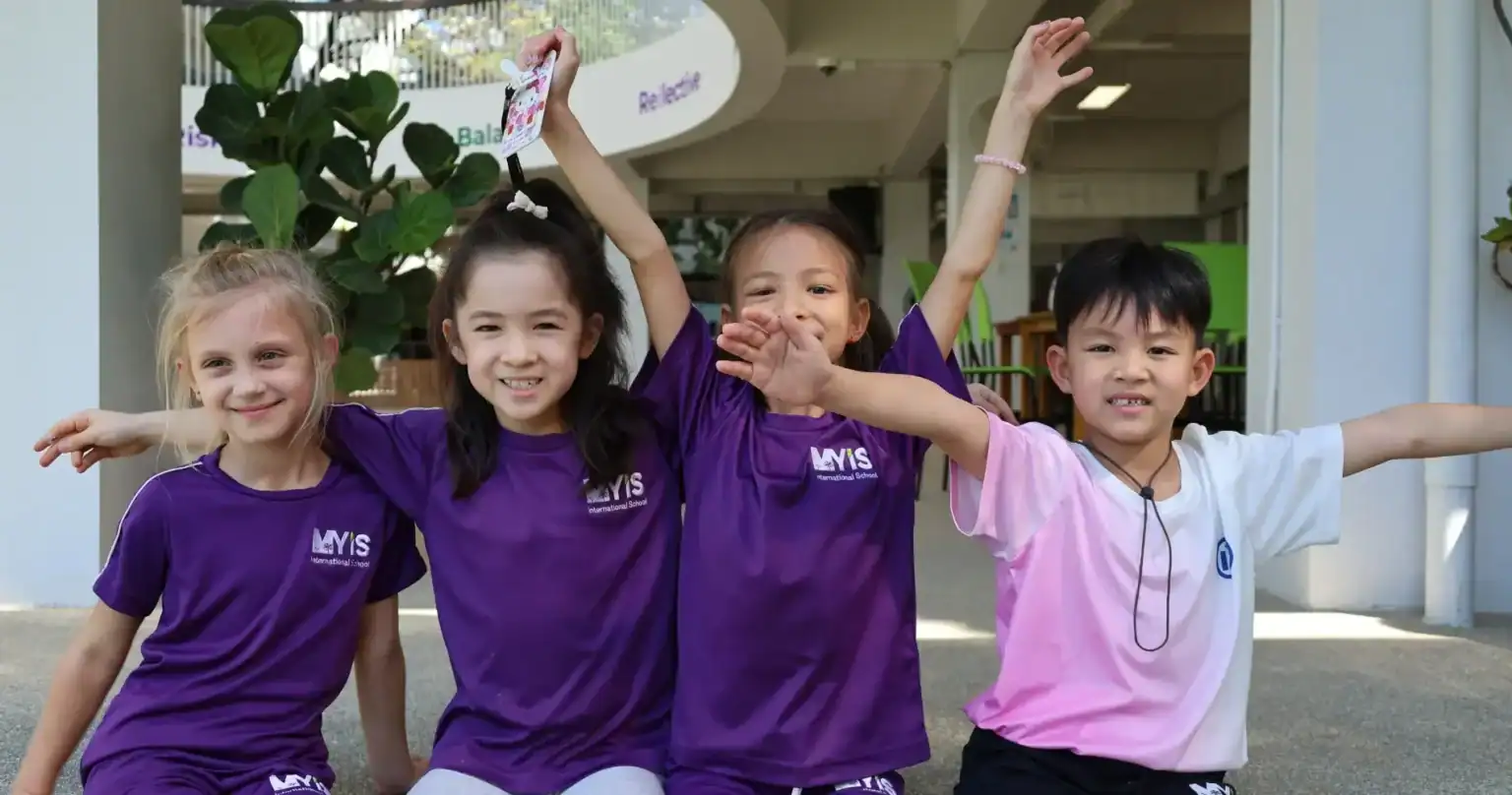 Group of happy students in MYIS International School uniforms outdoors.