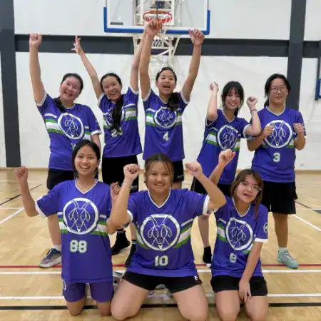 Girls' basketball team celebrating victory at MYIS International School gym.