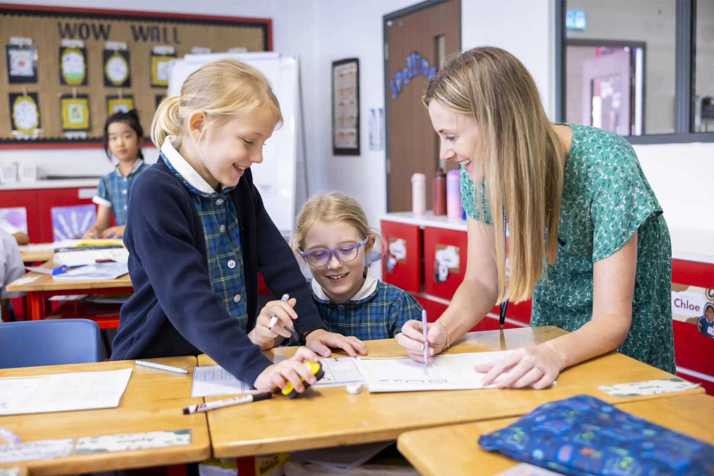 Happy schoolgirls and teacher collaborating in classroom with educational materials.