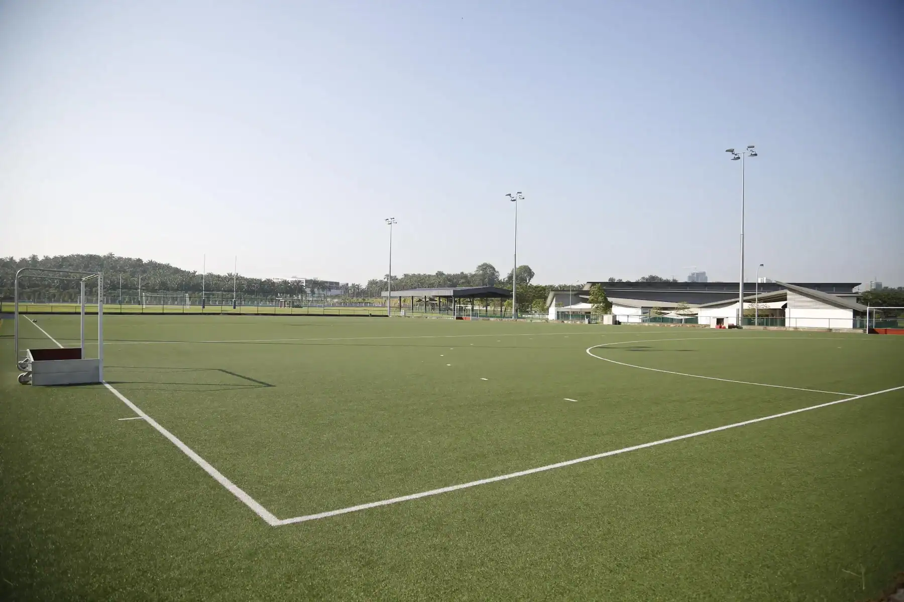 A lush green school sports field with goalposts and floodlights under a clear sky.