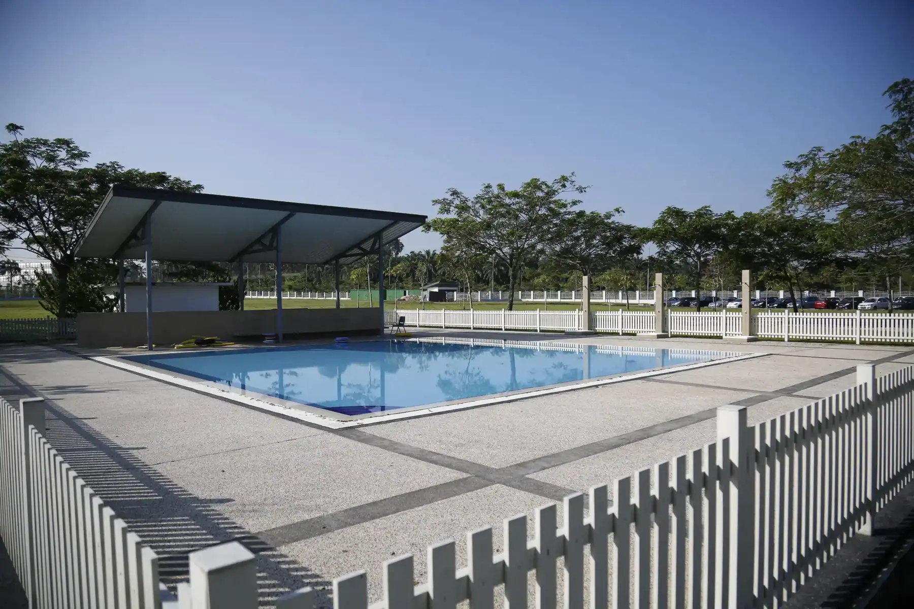Swimming pool at a modern school campus with shaded area and surrounding trees.