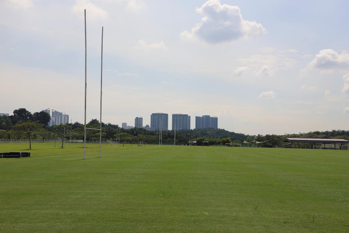 A lush green sports field with goalposts and a city skyline in the background.