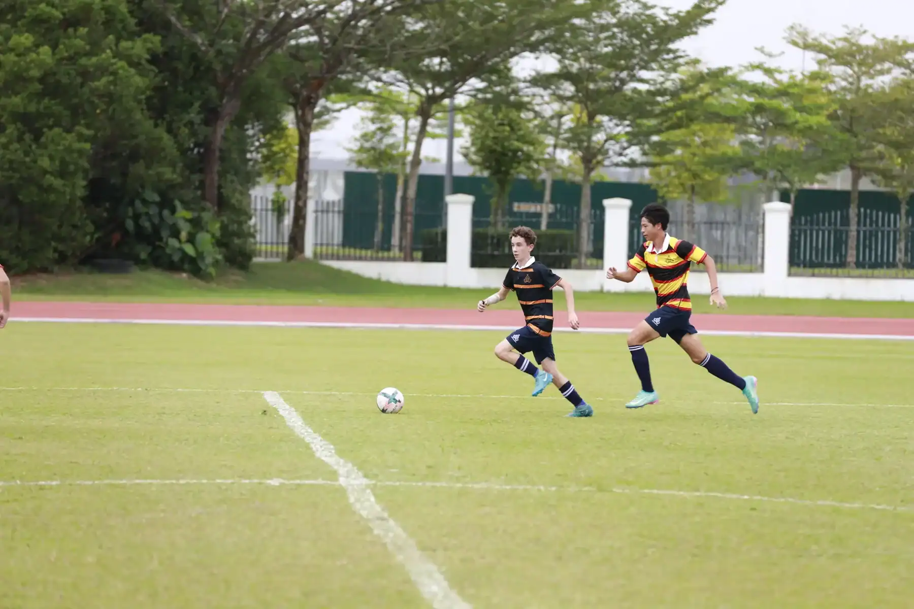 Young boys playing soccer on a school sports field during daytime.