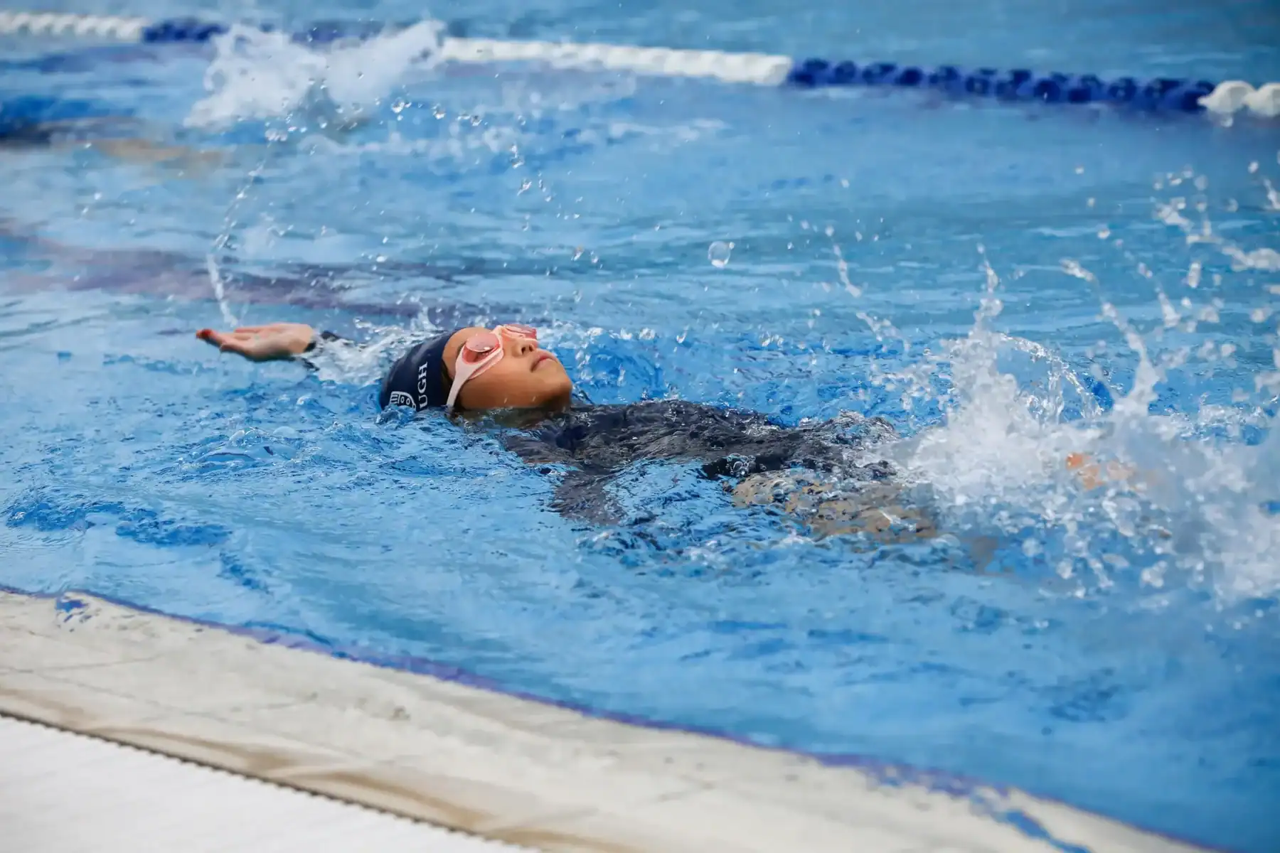 Swimming girl performing backstroke in a pool, practicing competitive swimming skills.