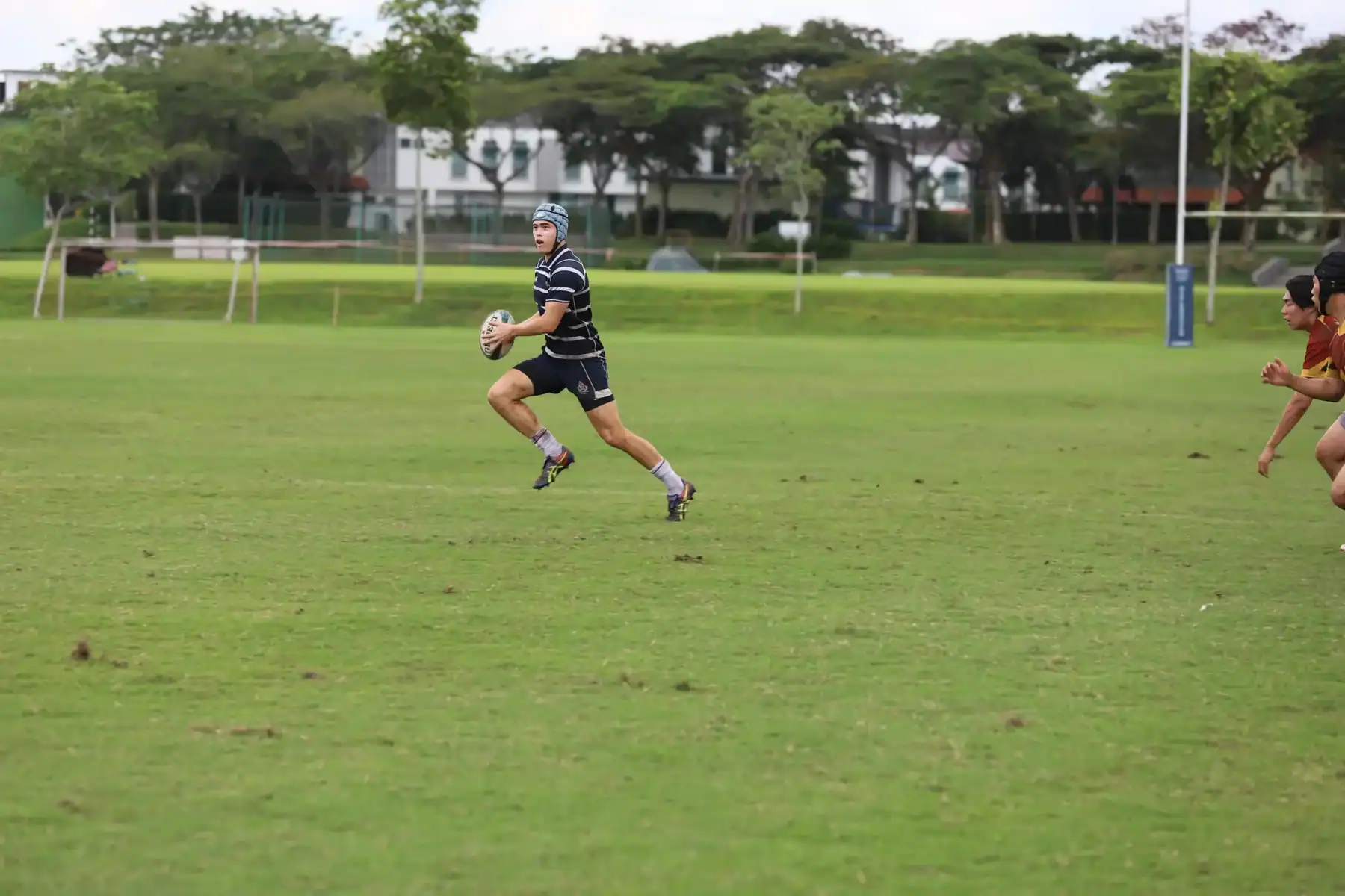 Young rugby player running with ball on green field during practice or game.