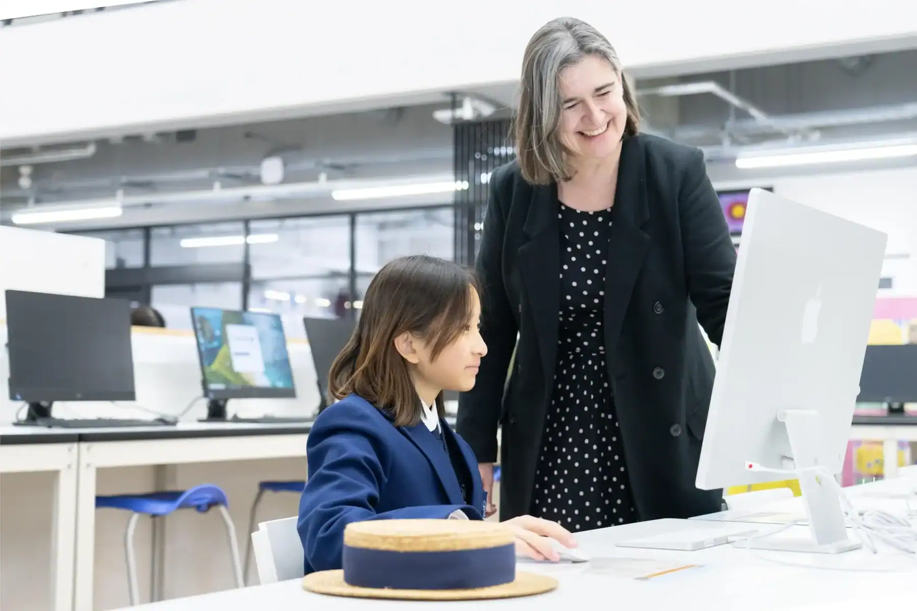 Teacher and student working together at a computer in a modern classroom.