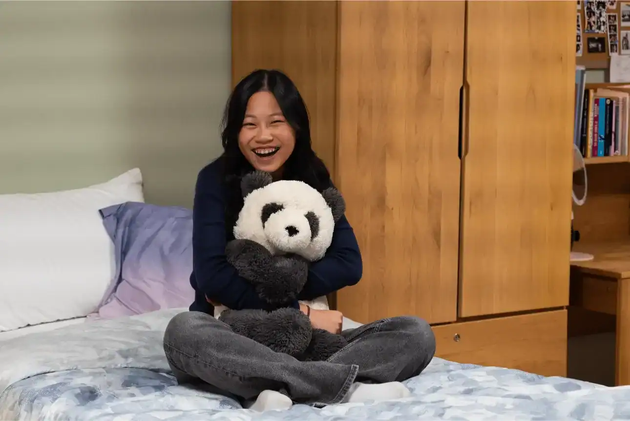 Happy girl with panda plush toy in a cozy bedroom at Harrow International School Appi Japan.