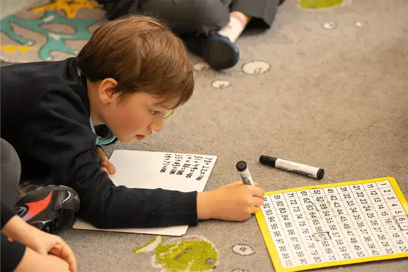Young student engaged in learning with a number chart and writing on paper.