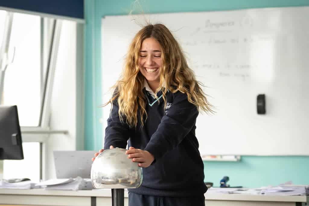 Student smiling while conducting a science experiment in classroom.