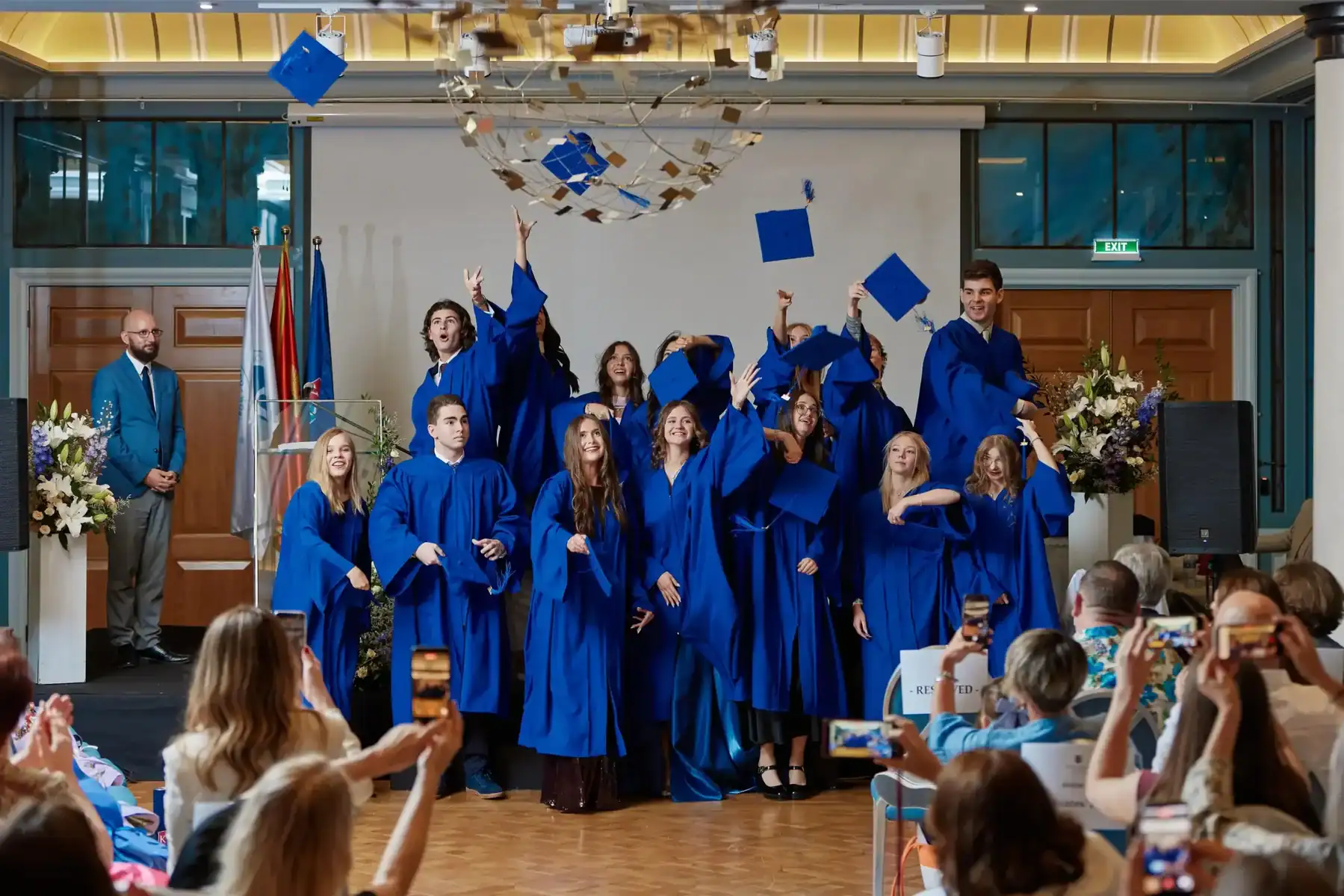 Graduates in blue caps and gowns celebrating at a school ceremony.