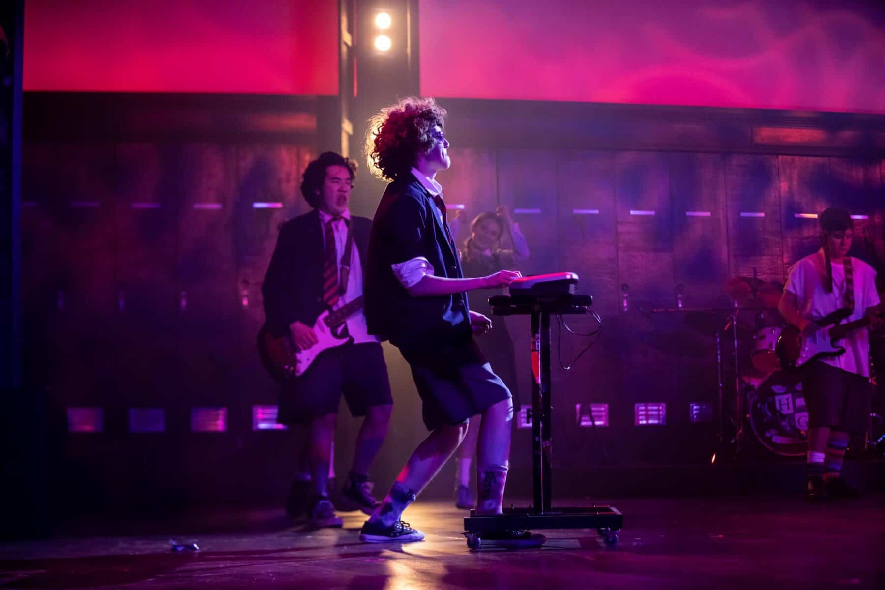 Students performing on stage with musical instruments and keyboard in a vibrant setting.