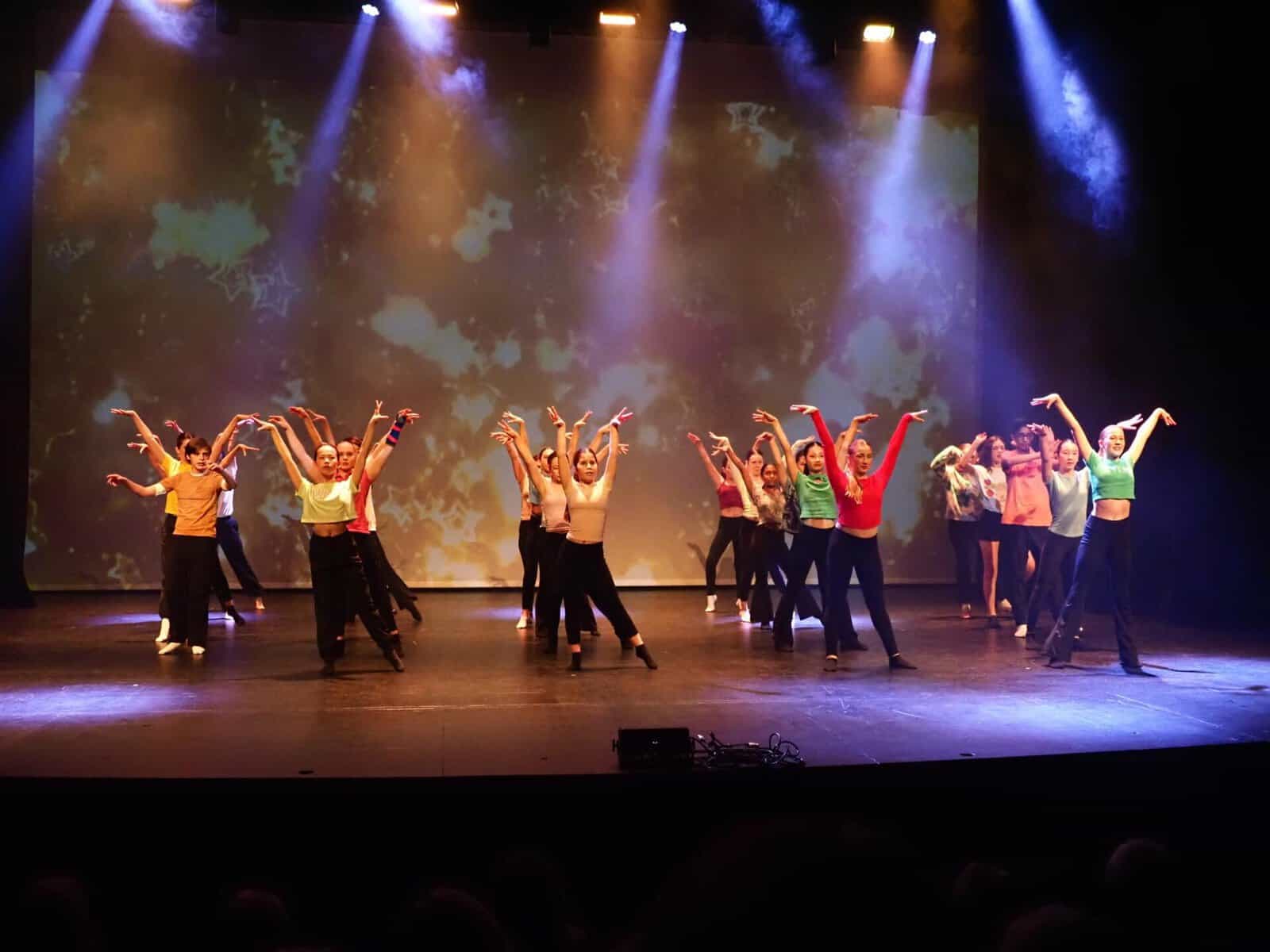 Group of students performing a dance on stage with colorful lighting.