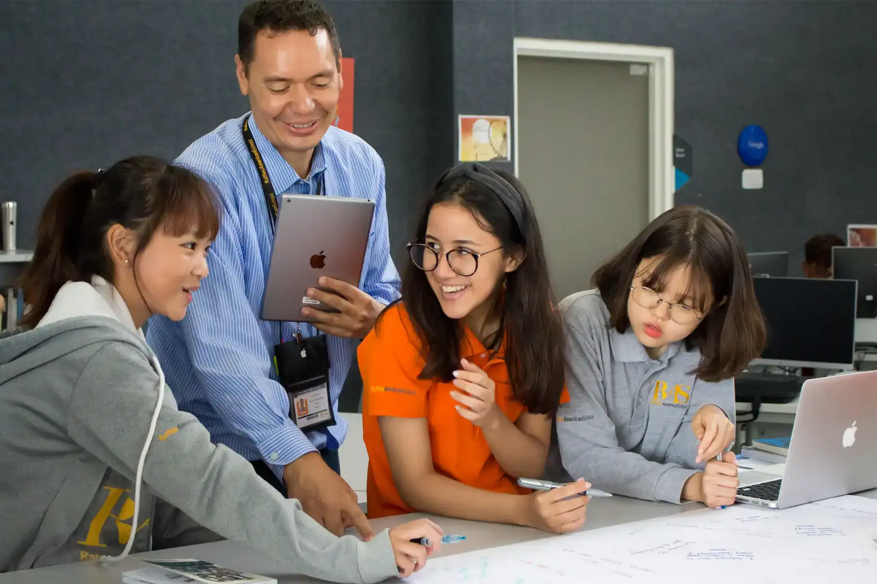 Students collaborating with teacher in a modern classroom at Raffles American School.