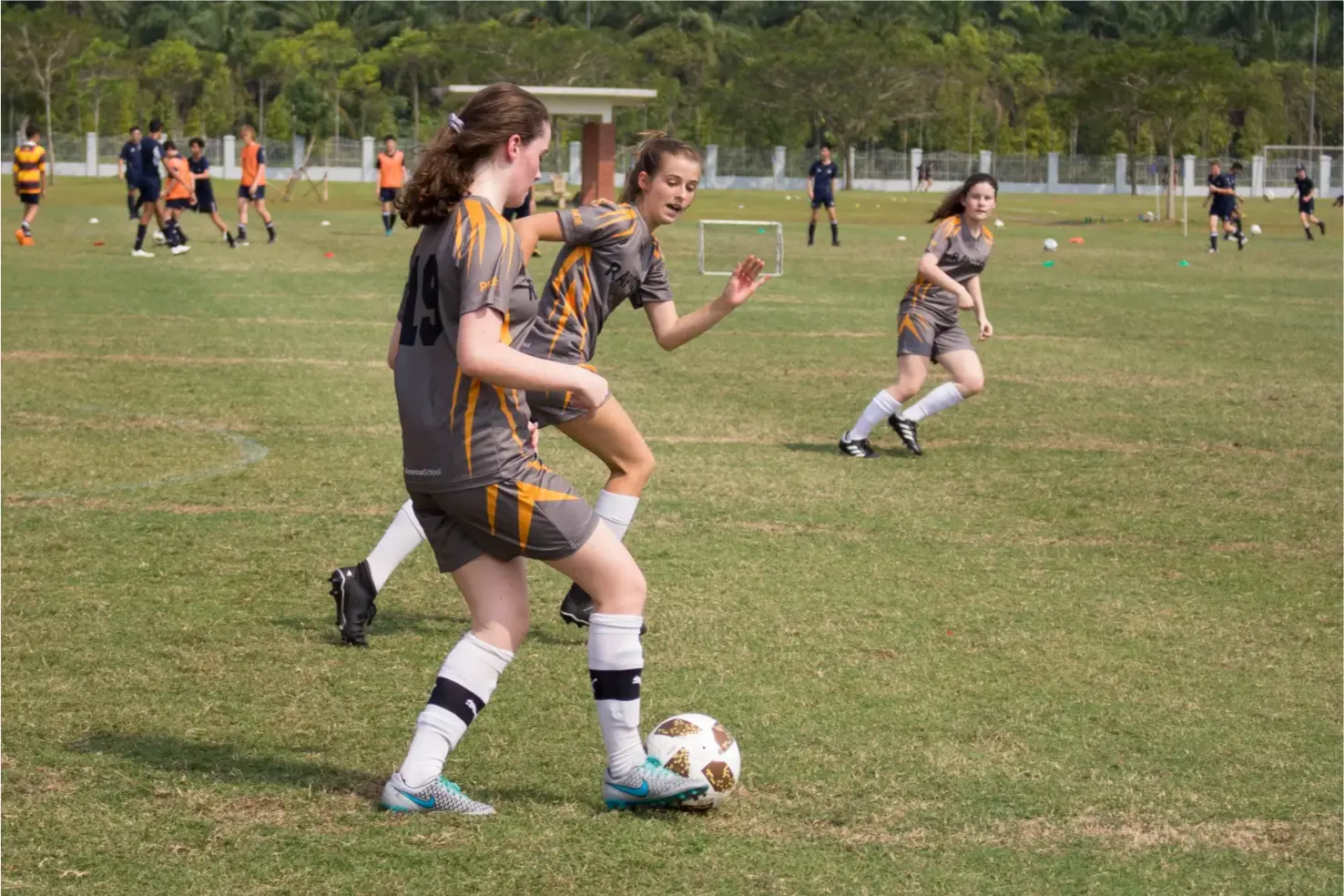 Girls playing soccer on a school field during a sports event.