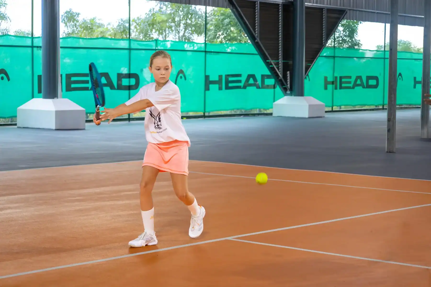 Young girl playing tennis indoors at Raffles American School.
