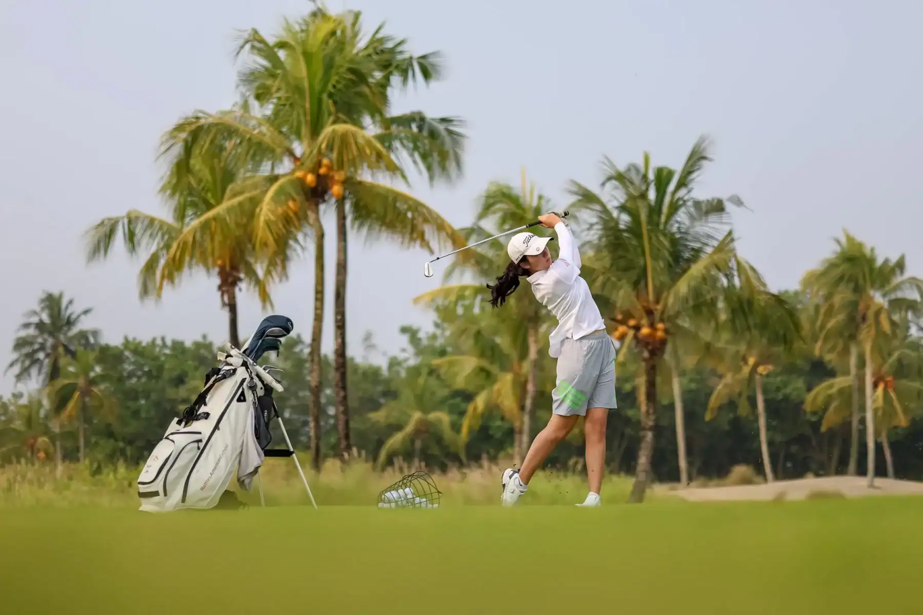 Young woman playing golf on a lush course with palm trees in the background.