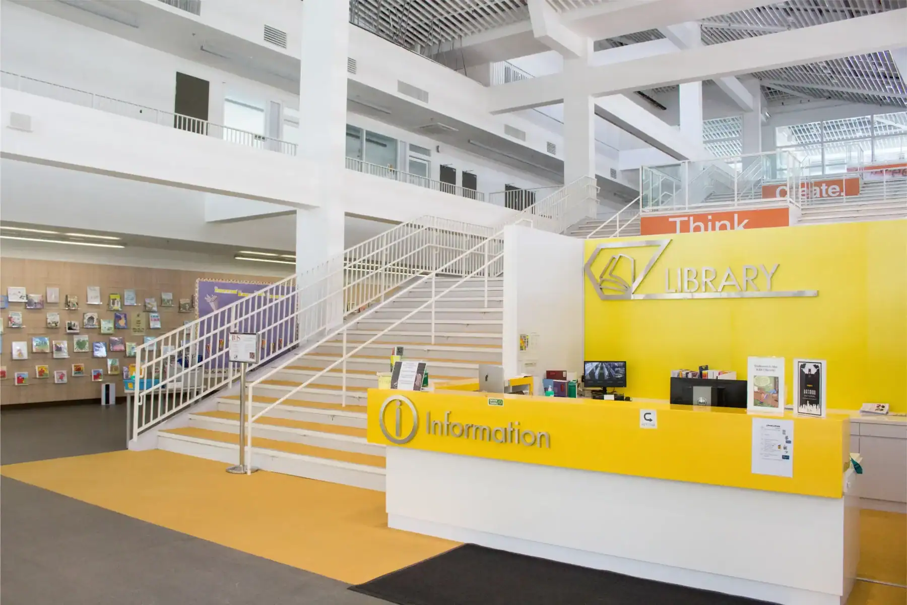 Modern school library with information desk and staircase in bright interior.