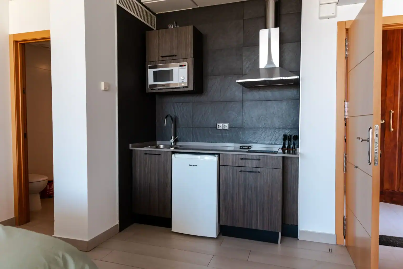 Compact modern kitchen with dark cabinetry and essential appliances in a contemporary school accommodation.